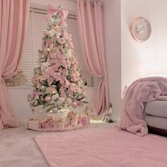 a pink christmas tree in the corner of a room with curtains and blankets on it