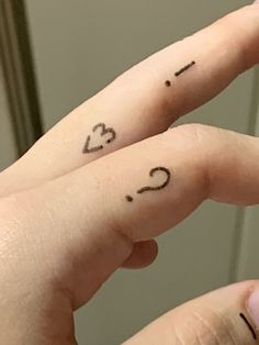 two fingers with small tattoos on them, one has the letter c and the other has the number 3