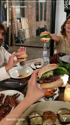 people sitting at a table with plates of food in front of them and one person holding up a hamburger