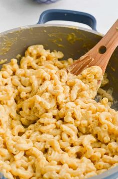 macaroni and cheese being stirred with a wooden spoon in a blue skillet