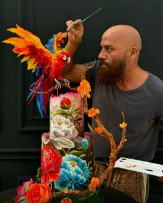 a man is painting a multi - colored cake with flowers and birds on it while holding a paintbrush