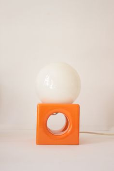 an orange and white lamp sitting on top of a wooden block next to a wall