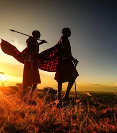 two women are standing in the grass at sunset