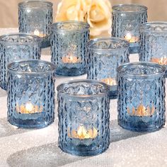 many blue glass candles are lined up on a white tablecloth with a flower in the background