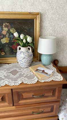 a vase with flowers on top of a dresser next to a lamp and painting in the background