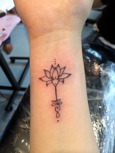 a small tattoo on the wrist of a woman with a cross and lotus flower in it