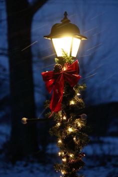 a street light decorated with christmas lights and a red bow on it's pole