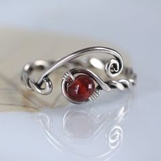 a silver ring with a red stone in it's center on a white surface