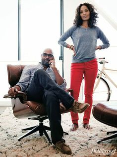 a woman standing next to a man sitting in an office chair while talking on a cell phone