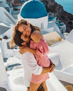 a man and woman hug each other on the roof of a building in oia