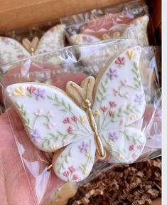 a hand is holding some cookies decorated like butterfly's wings and pink, purple, yellow and green flowers