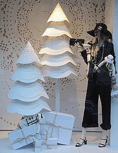 a window display with white christmas trees and presents in front of the store's mannequins