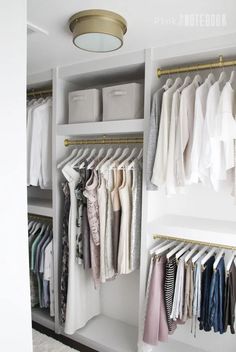 an organized closet with clothes hanging on shelves and folded shirts in bins, under a light fixture