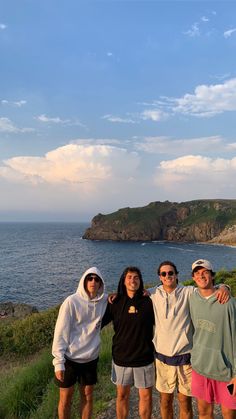 four people standing on the side of a road next to the ocean in front of an island