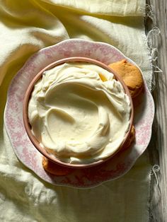 a pink and white plate topped with cream next to cookies on top of a yellow cloth