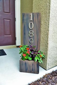 a house number sign sitting next to a planter with flowers in it on the front porch