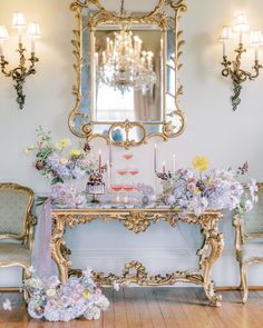 a table with flowers and candles on it in front of a mirror, chandelier and two chairs