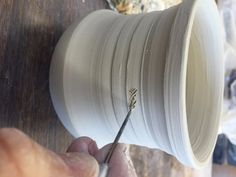 a person using a pair of scissors to trim a piece of white pottery on a wooden table