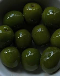 green apples are in a white bowl on the counter top, ready to be eaten