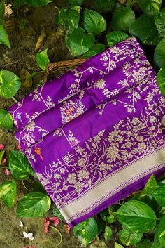 a purple and white cloth laying on top of green leaves