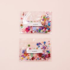 two clear bags filled with colorful sequins on top of a pink surface next to each other