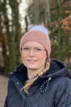 a woman wearing a pink hat and jacket in front of some trees with leaves on it