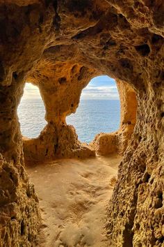 an open cave with water in the background and sand on the ground at the bottom