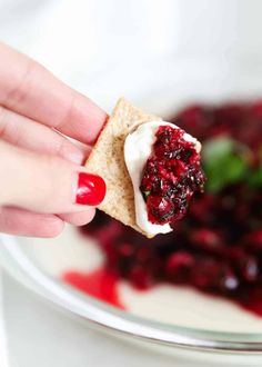 a hand holding a cracker with cranberry sauce on it