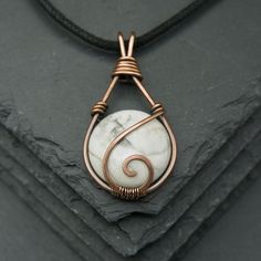 a white marble pendant with copper wire wrapped around it on top of a stone slab