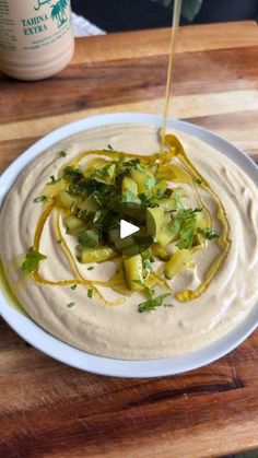 hummus being drizzled with olives and cilantro on a wooden cutting board