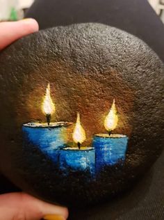 a person holding up a painted rock with three lit candles on it