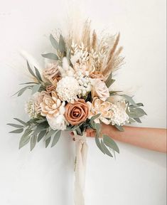 a bridal bouquet is held up against the wall by someone's hand with flowers on it