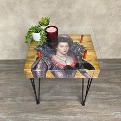 a wooden table with a glass top and a painting on it's surface next to a potted plant