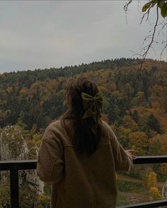 a woman standing on top of a balcony next to a forest