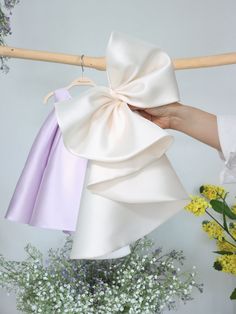 a hand holding a white bow on top of a purple dress hanging from a clothes line