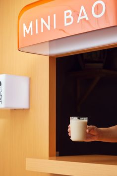 a person holding a cup in front of a sign that says minibao on it