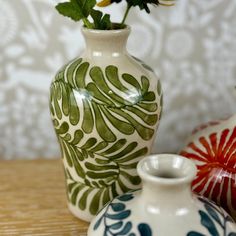 three vases with flowers in them sitting on a table next to wallpapered walls