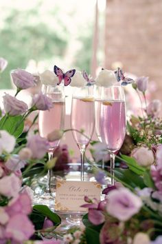 three glasses filled with pink liquid sitting on top of a table next to purple flowers