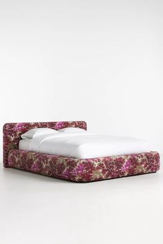 an upholstered bed with white sheets and pink flowers