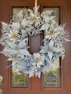 a wreath with silver flowers and leaves hanging on the front door to welcome guests into the house