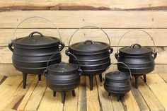 four black cast iron pots sitting on top of a wooden table next to each other