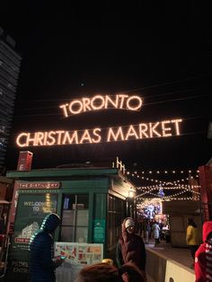 people are standing in front of a christmas market at night with lights on the building