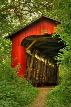 a red covered bridge surrounded by trees and bushes