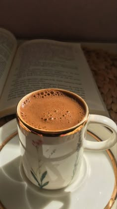 a cup of hot chocolate sitting on top of a saucer next to an open book