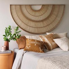 a bed topped with lots of pillows next to a potted plant on top of a table