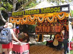 some people are standing under a tent with tattoos on it and there is a sign that says neata's henna tatoos