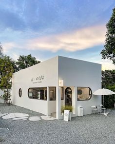 a white building sitting on top of a gravel field next to trees and umbrellas