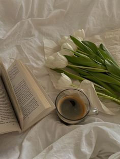 a cup of coffee next to an open book and some tulips on a bed