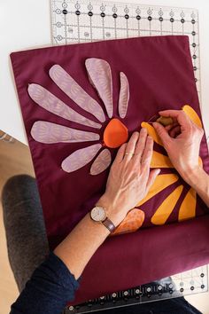 a woman is working on a piece of art with her hands and sewing machine in the background