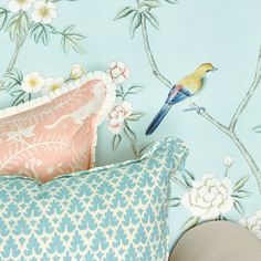 a blue and yellow bird sitting on top of a pillow in front of a floral wallpaper